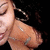 A close-up of a person's face with closed eyes, wearing a large hoop earring and a silver necklace, against a black background.