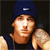 Pixelated image of a person wearing a dark blue beanie with a small white rectangular logo, a sleeveless dark shirt, and light brown skin, set against a dark background.
