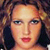 Pixelated close-up of a person's face with light skin, dark eyes, and red lips, set against a blurred background of warm tones.