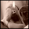 A sepia-toned close-up of a person holding a silver Zippo-style lighter with a visible flame, wearing a bracelet and denim fabric.