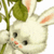 Pixelated bunny with white fur, black eyes, and pink inner ears holding green leaves against a plain background.