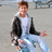 Pixelated static image of a person with light brown hair wearing a white shirt and dark jacket, standing against a neutral background with one hand extended.