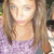 Pixelated close-up of a person with long light brown hair, wearing a light purple patterned top, against a blurred background.