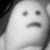 Static grayscale pixelated image of a face with two square eyes and a downturned mouth, set against dark background elements.