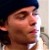 Pixelated close-up of a person's face in profile, wearing a dark blue cap, with visible skin tones and blurred background elements.