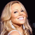 Pixelated close-up of a smiling person with long blonde hair against a black background, wearing a white strap top.