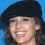 A static image shows a person with curly brown hair wearing a black beret against a solid blue background, with text elements below.