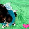 A pixelated image shows a person with dark hair wearing a blue top and white shoes, leaning forward on a green background with a pink heart symbol.