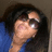 Pixelated image of a person with dark hair wearing sunglasses and blue clothing, holding an object near their face.
