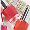 Red and orange nail polish bottles with metallic caps arranged on a striped fabric background.
