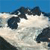 Pixelated image of a dark-colored vehicle on a light surface under a blue sky, with no visible text or distinct motion.
