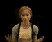 Animated sequence of a person with light brown hair in braids wearing a gray cardigan over a yellow graphic t-shirt against black background.