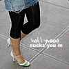 A cropped image shows a person's lower legs and feet wearing black capri pants, white high-heeled shoes with green and blue accents, and a light blue denim garment, standing on a gray tiled surface with overlaid text.