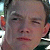 A pixelated close-up of a person's face with closed eyes, showing a neutral expression, partially visible ear, and dark clothing collar.