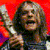 Pixelated static image of a person with long hair against a red background, wearing dark clothing and holding an object near their face.