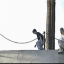 A sequence of showing a person performing a skateboard trick on a concrete ledge with metal railings, transitioning from standing to mid-air jump