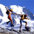 Pixelated static image of two stick figures on a snowy slope with blue sky background, one figure holding a flagpole and the other appearing to ski or climb.