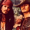 Two men in pirate costumes pose together, one with a red bandana and long dark hair, the other with a wide-brimmed hat and a mustache.
