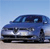 Blue sedan car with visible headlights and grille, positioned on a light brown surface under a gradient blue sky background.