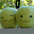 Two green cartoon apples with smiling faces, one winking, set against a blurred green background with a small green vertical bar above.