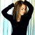 A 50x50 pixel animated contact sheet showing two frames of a woman with long brown hair wearing a black top, first adjusting her hair with both hands and then placing one hand on her chest.