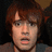 Pixelated close-up of a person with brown hair and light skin, wearing a dark shirt against a dark background.