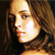 Pixelated close-up of a person's face with light brown hair, warm lighting, and a dark background.