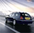 A pixelated image of a dark-colored vehicle with visible headlights and a yellow section on the side, set against a light sky background.