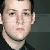 Static pixelated image of a person's face with light skin, dark hair, and a neutral expression against a dark background.