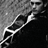 Black-and-white pixelated image of a person in profile wearing dark clothing with light trim, set against a gradient background.