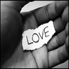 Black-and-white image of a hand holding a small torn paper fragment with the word LOVE written in bold letters.