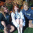 Pixelated static image of three figures in a group pose with blurred background colors.