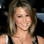 A pixelated close-up of a smiling person with light brown hair, wearing a dark top with white straps and a thin necklace.