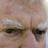 A pixelated close-up of a person's face with visible eyes and forehead, paired with text elements on black backgrounds.