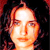 Pixelated close-up of a person's face with light skin tone, dark hair, and neutral expression against dark background.