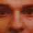 A pixelated close-up of a face with brown eyes, nose, and mouth against an orange-brown background.