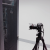 A pixelated figure holding a camera on a tripod against a light background with a dark vertical element.