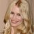 Pixelated close-up of a smiling person with long blonde hair against a light brown background.