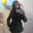 Pixelated image of a person with long dark hair wearing a black coat, standing outdoors near a light-colored structure with a yellow object in the background.