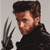 Pixelated image of a person with short brown hair wearing a black high-collared jacket, holding a dark clawed hand near their face against a light gray background.