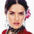 Static pixelated image of a person with dark hair styled in an updo, wearing red clothing and a pink flower accessory behind the ear.