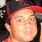 Pixelated close-up of a person wearing a red and black cap, light skin tone, and dark hair visible beneath the cap.