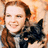 A pixelated image shows a person with light brown hair holding a small black dog against an orange and beige background.