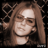 A sepia-toned image of a person with long brown hair and sunglasses, positioned behind a chain-link fence, with the word 'AVRIL' in pixelated text below.