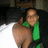 Pixelated image of a person with light skin wearing green clothing, holding an object against a dark background.