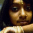 Pixelated close-up of a person with dark hair and light skin, wearing a white top against a dark background.