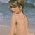Static pixelated image of a shirtless person with short brown hair standing against a blurred beach background, rendered in low-resolution 256x256 pixels.
