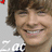 Pixelated close-up of a smiling person with brown hair, wearing dark clothing and white text on the chest.