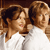 Three figures with brown hair in white shirts, positioned closely together against a dark brown background.