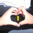 A hand forms a heart shape with fingers, displaying yellow text inside the heart against a dark background.